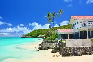 Turquoise water butting up to a stone retaining wall outside of a house. Palm trees and lush mountains in the background
