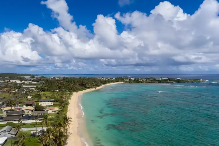 Aerial view of Oahu coastline showing homes and beach, renting vs buying on Oahu